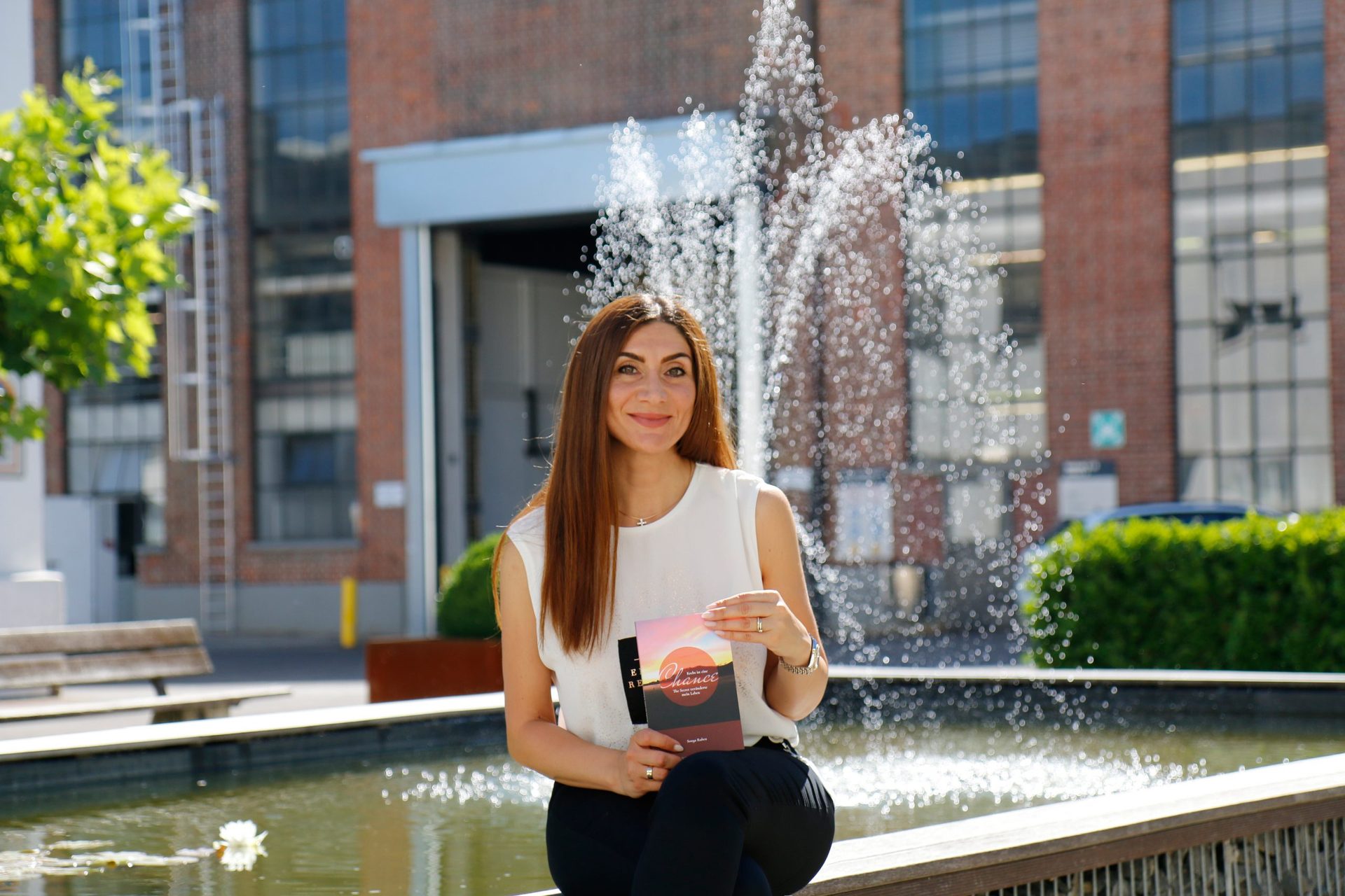 Sonya Ruben sitzt lächelnd mit ihrem Buch am Brunnen